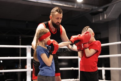 Photo of Children practicing fight on boxing ring under their coach supervision