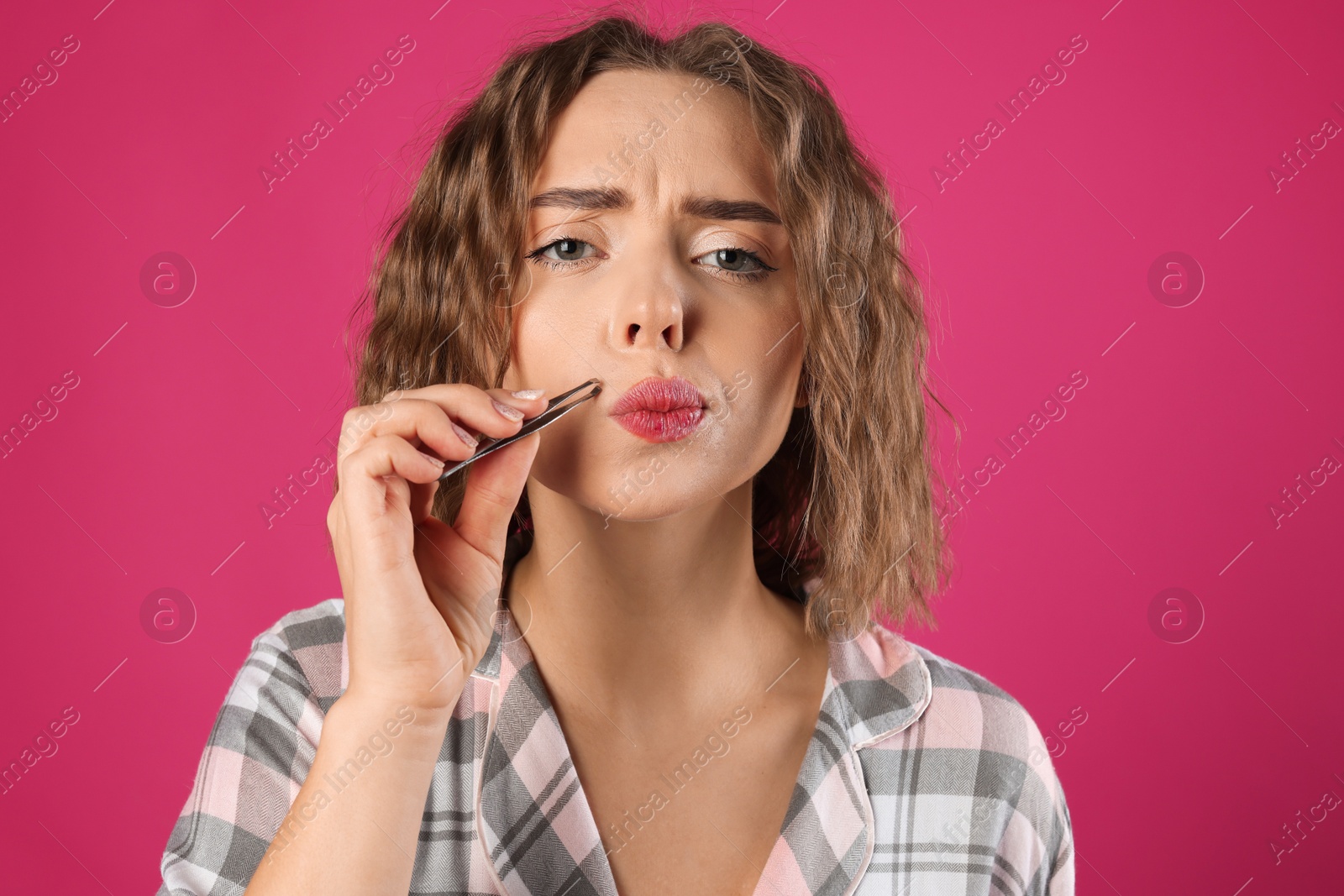 Photo of Beautiful woman plucking her mustache with tweezers on pink background