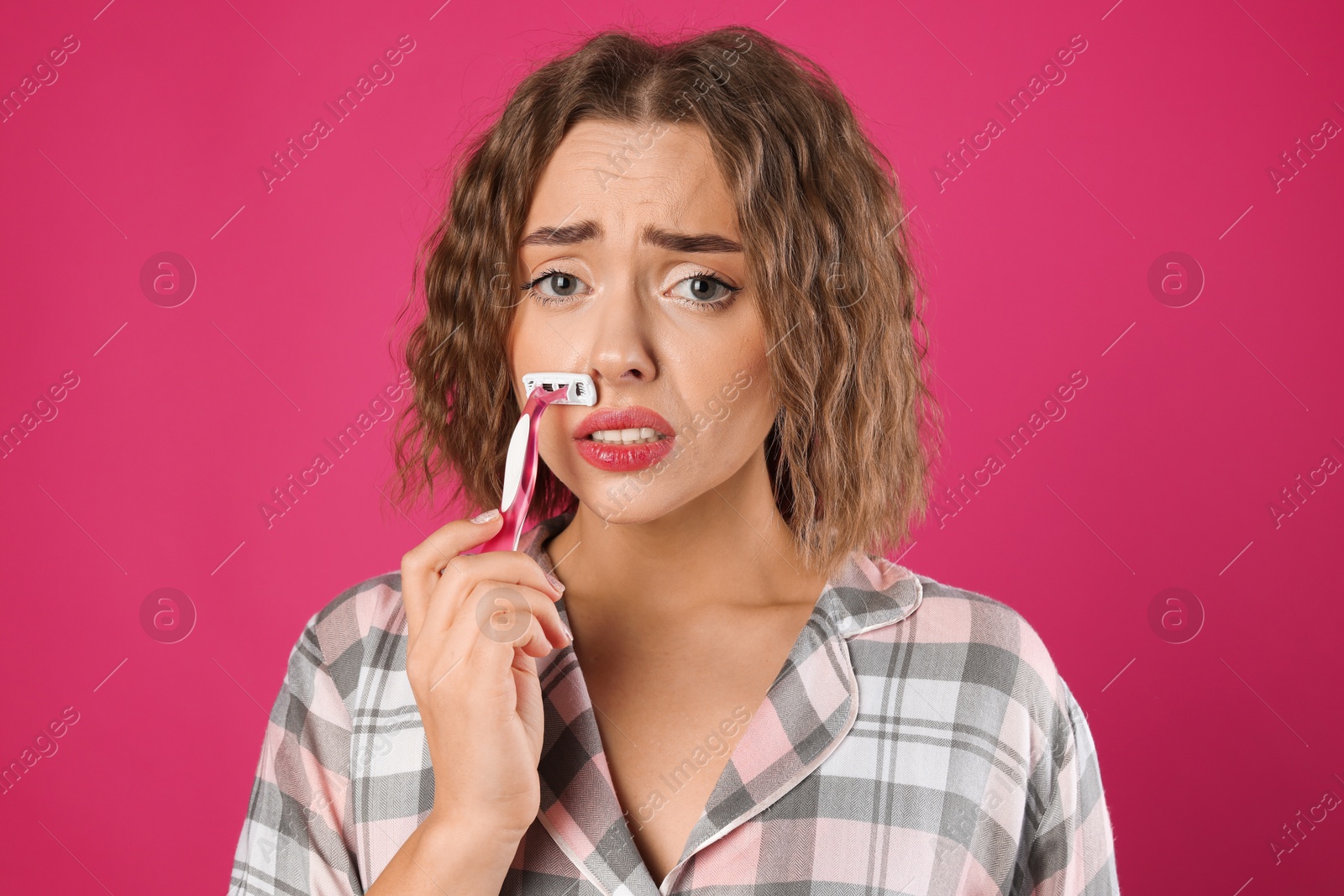 Photo of Emotional woman shaving her mustache with razor on pink background