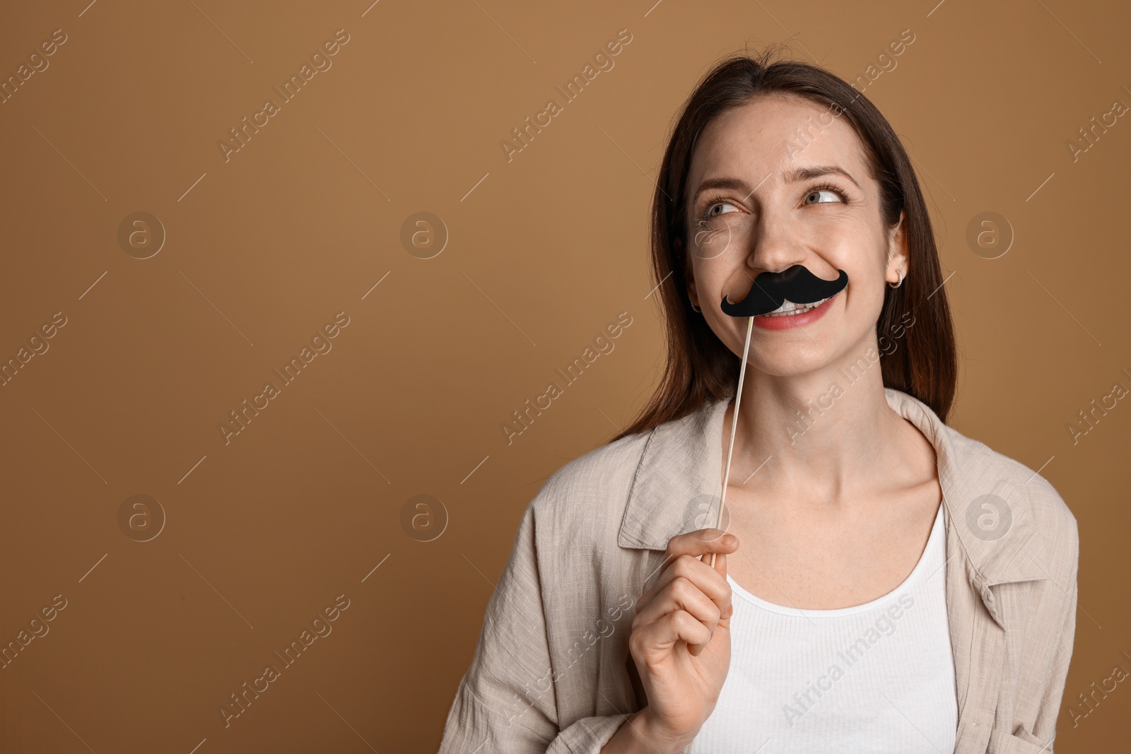 Photo of Happy woman with fake paper mustache on brown background. Space for text