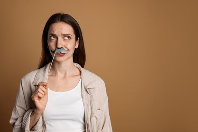 Thoughtful woman with fake paper mustache on brown background. Space for text