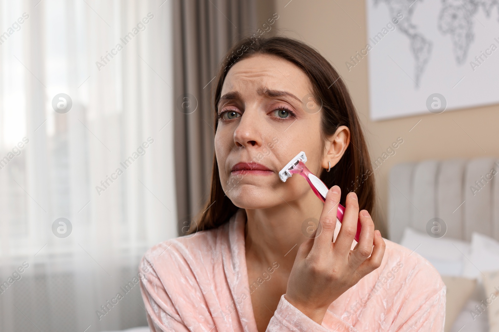 Photo of Beautiful woman shaving her mustache with razor at home