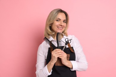 Smiling hairdresser with combs and brush on pink background