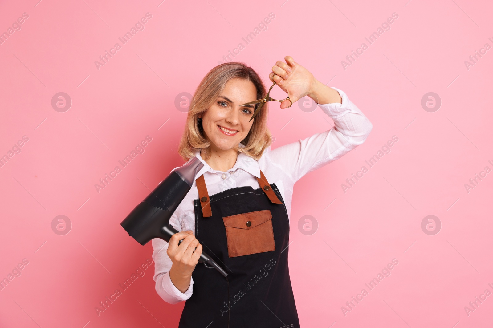 Photo of Smiling hairdresser with dryer and scissors on pink background