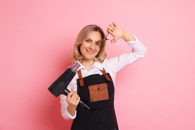 Photo of Smiling hairdresser with dryer and scissors on pink background