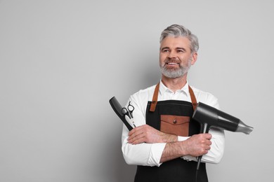 Photo of Smiling hairdresser with dryer, scissors and comb on gray background, space for text