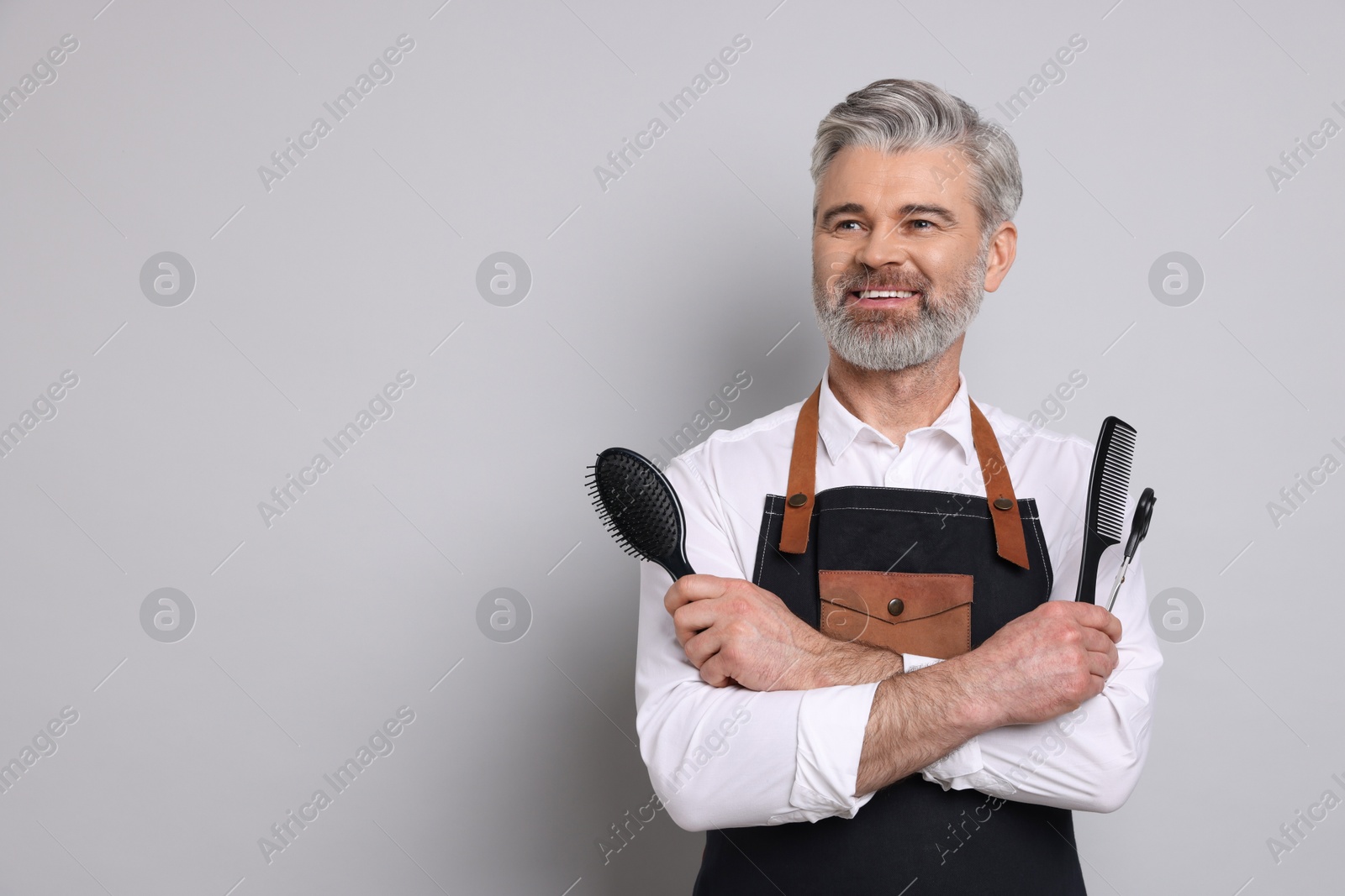 Photo of Smiling hairdresser with brush, scissors and comb on gray background, space for text