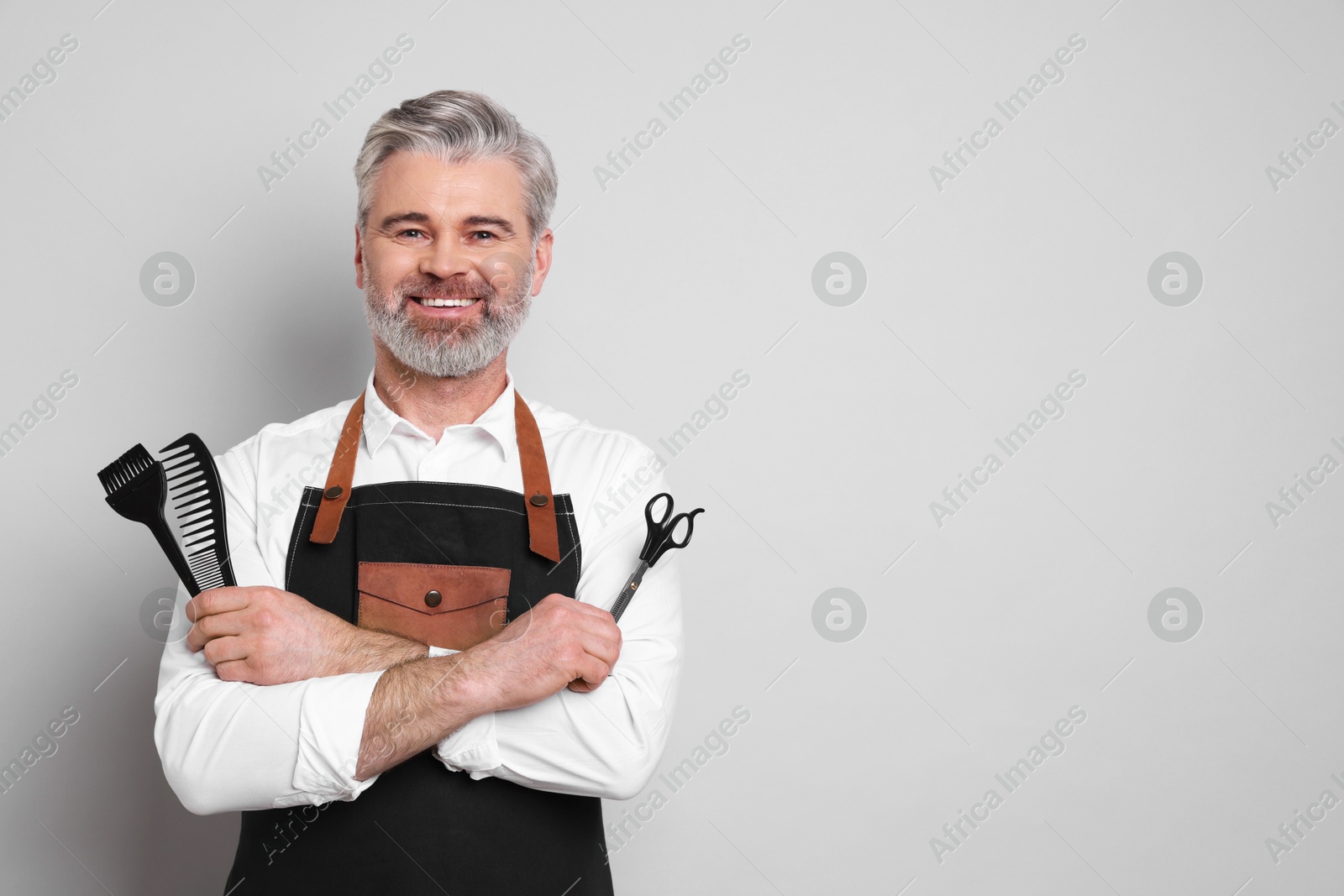 Photo of Smiling hairdresser with scissors, comb and hair dye brush on gray background, space for text