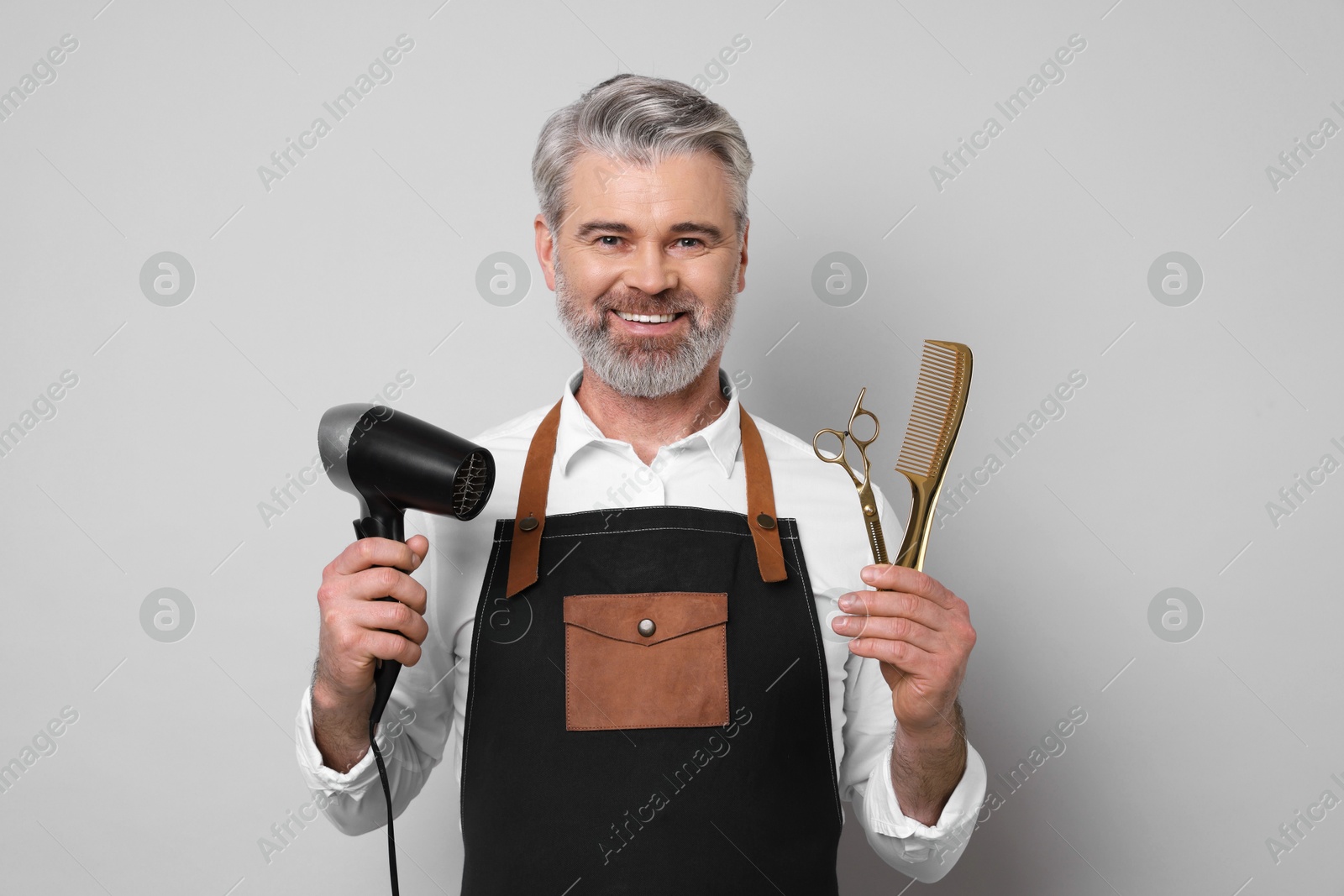 Photo of Smiling hairdresser with dryer, scissors and comb on gray background