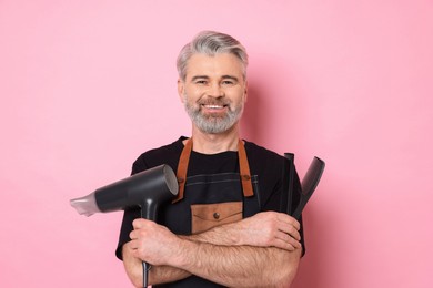 Photo of Smiling hairdresser with dryer and combs on pink background