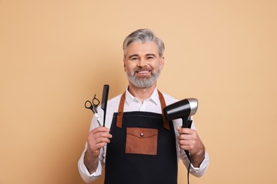 Photo of Smiling hairdresser with dryer, scissors and comb on beige background