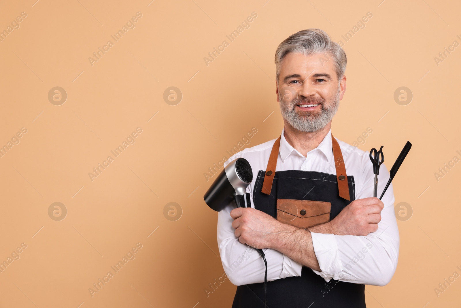 Photo of Smiling hairdresser with dryer, scissors and comb on beige background, space for text