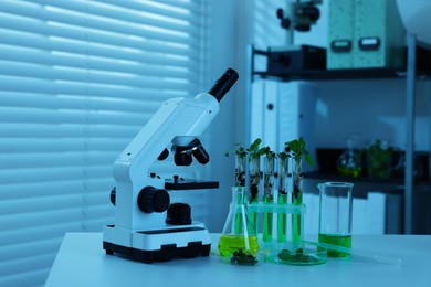 Photo of Biochemistry. Microscope, glassware with liquids and plants on white table in laboratory