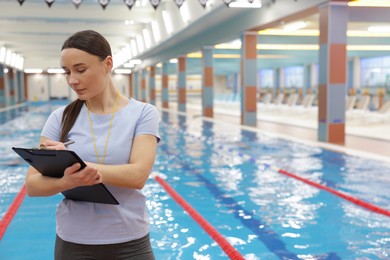 Photo of Swimming coach with clipboard taking notes at indoor pool. Space for text