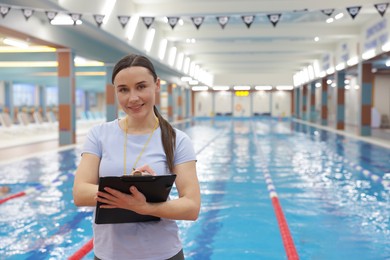 Photo of Swimming coach with clipboard taking notes at indoor pool. Space for text