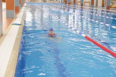 Woman wearing cap and goggles swimming in pool indoors