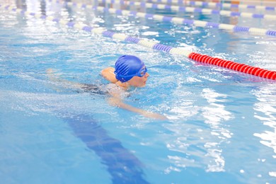 Woman wearing cap and goggles swimming in pool indoors