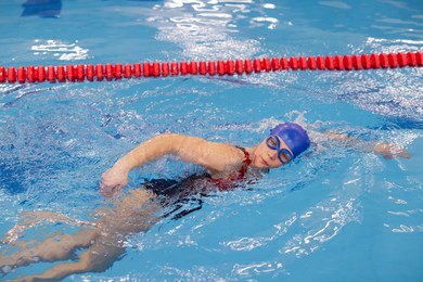 Sporty woman wearing cap and goggles swimming in pool indoors