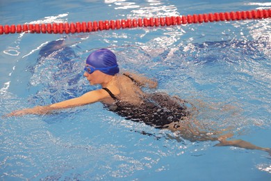 Photo of Sporty woman wearing cap and goggles swimming in pool indoors