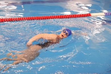 Sporty woman wearing cap and goggles swimming in pool indoors