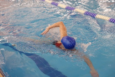 Woman wearing swimsuit, cap and goggles swimming in pool indoors