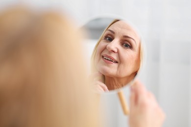 Photo of Smiling middle aged woman with round mirror on blurred background