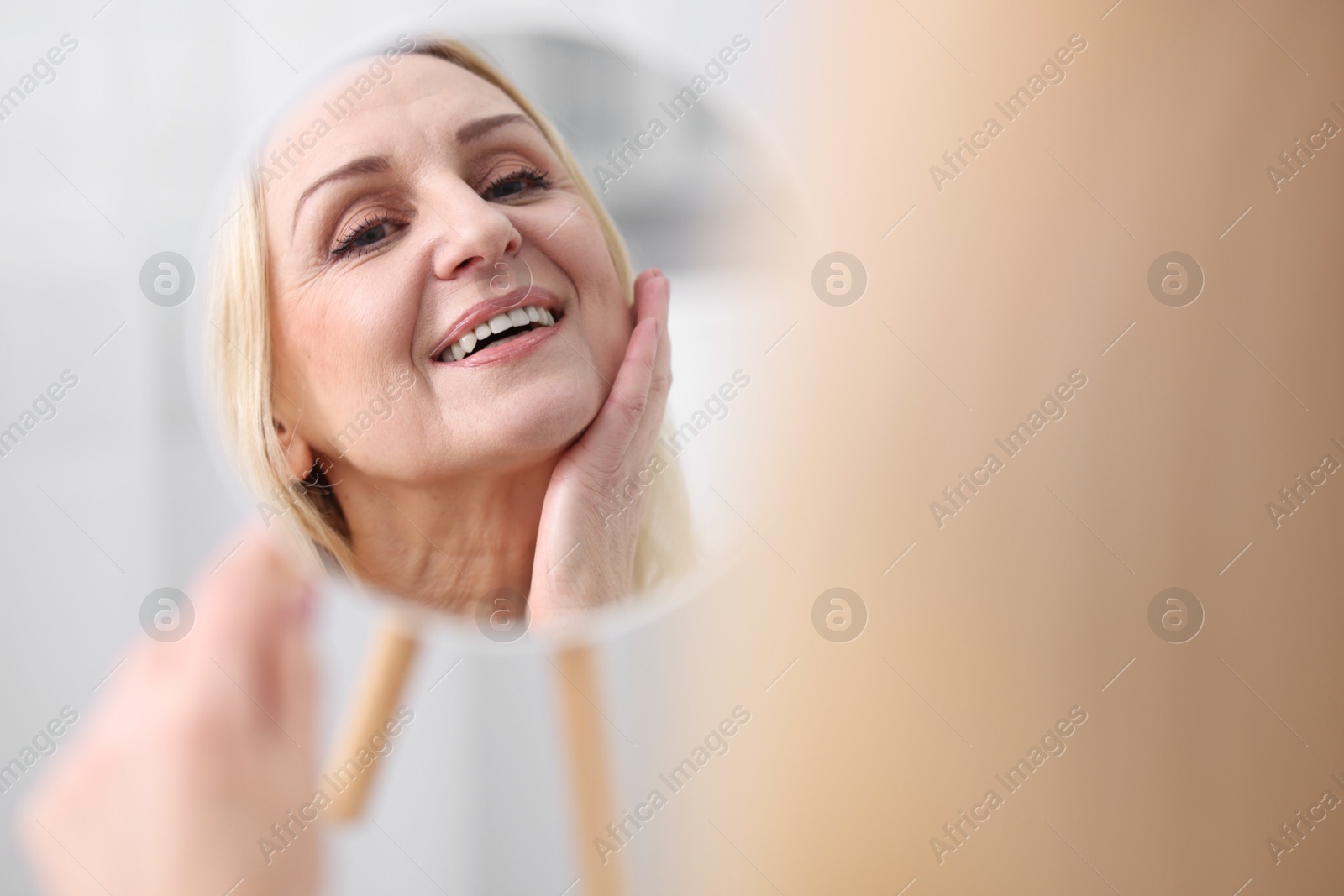 Photo of Smiling middle aged woman with round mirror on blurred background