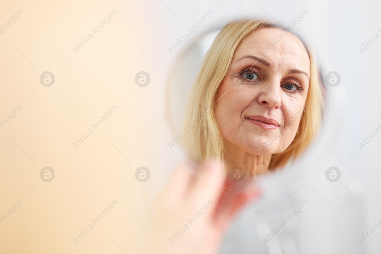 Photo of Beautiful middle aged woman with round mirror on blurred background