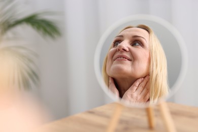 Photo of Smiling middle aged woman near round mirror on blurred background. Space for text