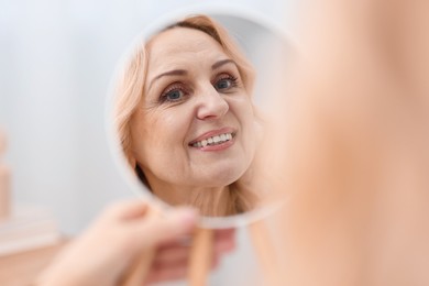 Photo of Smiling middle aged woman with round mirror on blurred background