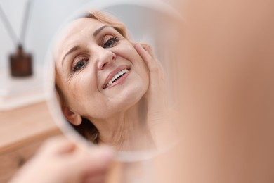 Photo of Smiling middle aged woman with round mirror at home