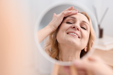 Photo of Smiling middle aged woman with round mirror at home