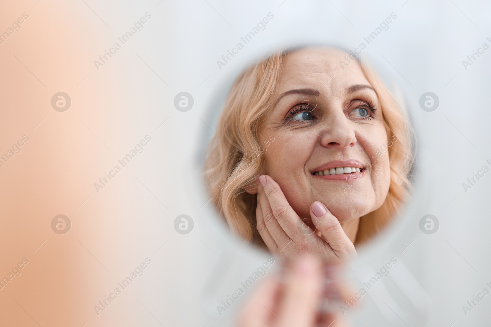 Photo of Smiling middle aged woman with round mirror on blurred background