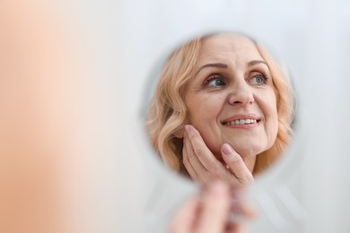 Photo of Smiling middle aged woman with round mirror on blurred background