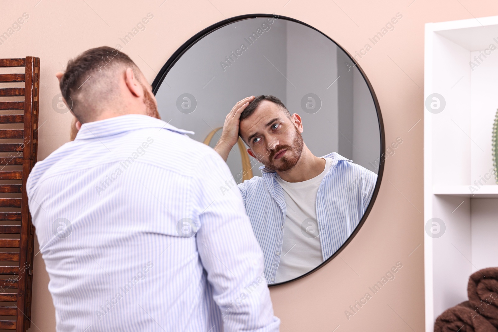 Photo of Baldness problem. Man with receding hairline near mirror in bathroom