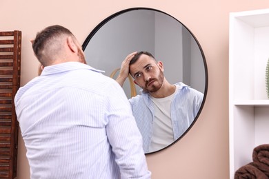 Photo of Baldness problem. Man with receding hairline near mirror in bathroom