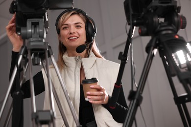 Photo of Happy young camerawoman with coffee working in modern film studio