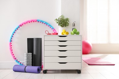 Photo of Different fitness equipment and chest of drawers indoors