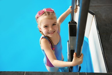 Photo of Little girl with goggles getting out of swimming pool indoors, space for text