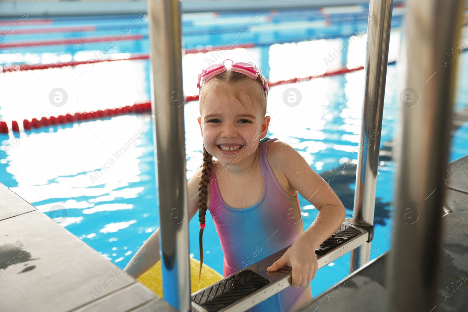 Photo of Little girl with goggles getting out of swimming pool indoors