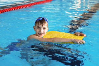 Boy with goggles and kickboard swimming pool indoors