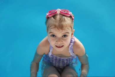 Photo of Little girl with goggles swimming in pool, above view