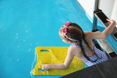 Photo of Little girl with goggles and kickboard swimming in pool, above view