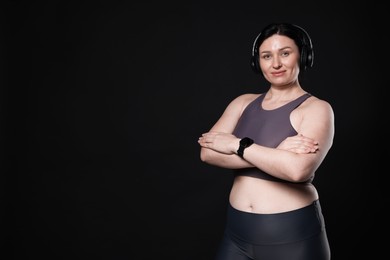 Plus size woman in gym clothes and headphones on black background, space for text