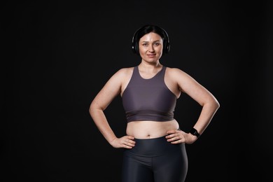 Plus size woman in gym clothes and headphones on black background