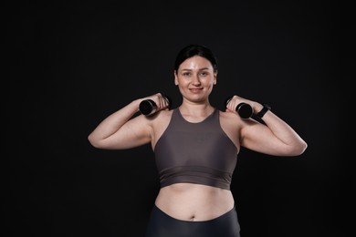 Plus size woman in gym clothes doing exercise with dumbbells on black background