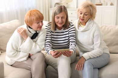 Photo of Senior woman showing something on smartphone to her friends at home