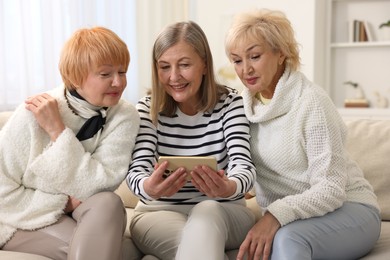 Photo of Senior woman showing something on smartphone to her friends at home