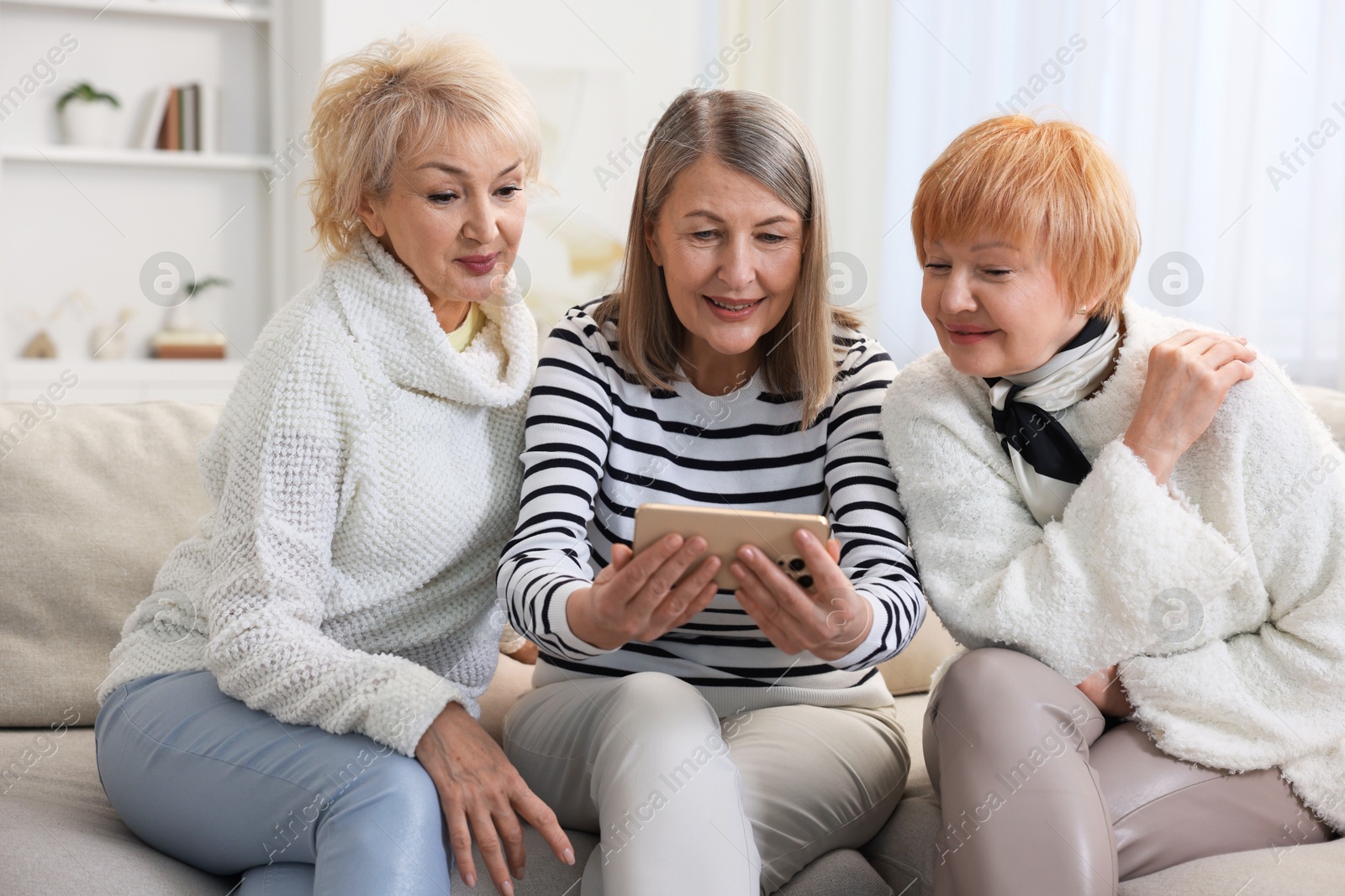 Photo of Senior woman showing something on smartphone to her friends at home