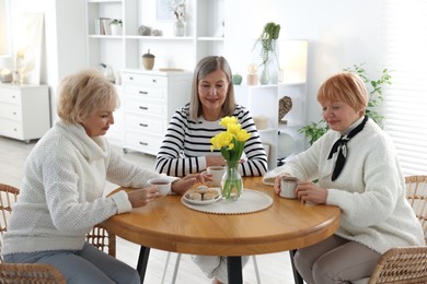 Photo of Friendship. Senior women enjoying hot drinks at table indoors